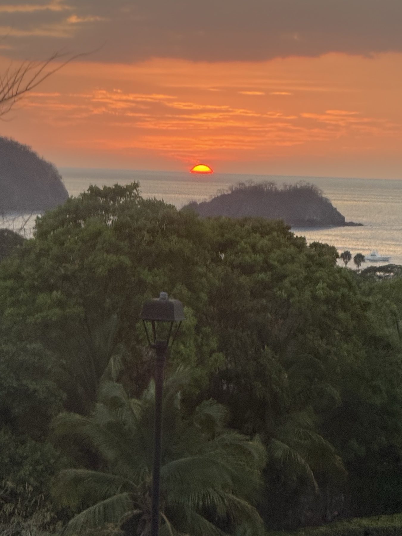 The sun setting into the Pacific behind the islands of Playas del Coco bay, seen over the treetops